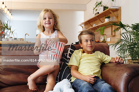 Children relaxing with popcorn on sofa at home