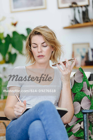 Businesswoman using cellular phone and writing notes in office