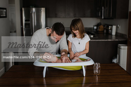 Young man and his daughter bathing baby son in kitchen