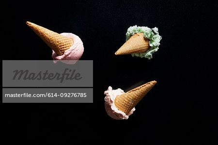 Three ice-cream cones, mint, chocolate chip and strawberry against black background, overhead view