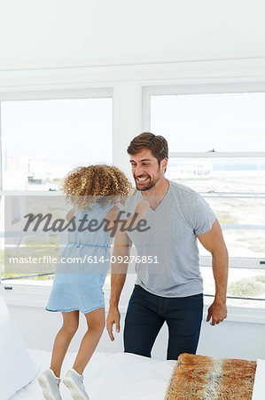 Father playing with daughter jumping on bed in beach house