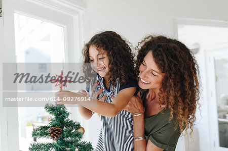 Mother helping daughter place star on Christmas tree at home