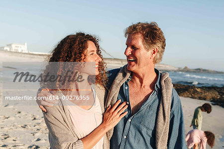 Couple taking walk on sandy beach, children in background