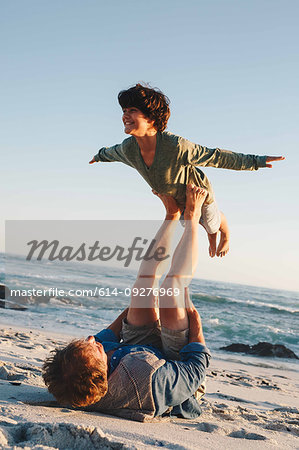 Father lifting son in mid air with legs on beach