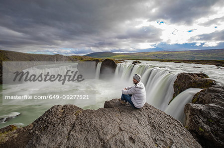 Man sitting on edge of rock, Godafoss waterfall, Bárðardalur, Iceland Man sitting on edge of rock, Godafoss waterfall, Bárðardalur, Iceland
