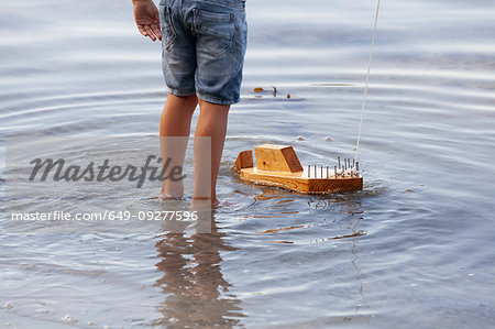 Boy playing with wooden toy boat in water