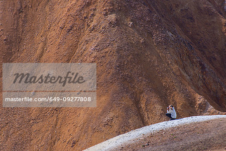 Hiker taking photograph on peak, Brennisteinsalda and Bláhnjúkur, Landmannalaugar, Highlands, Iceland