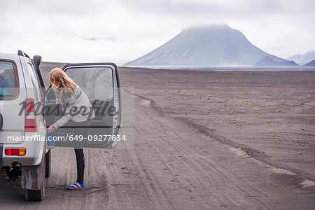 Woman changing shoes by vehicle door on dirt track, Landmannalaugar, Iceland
