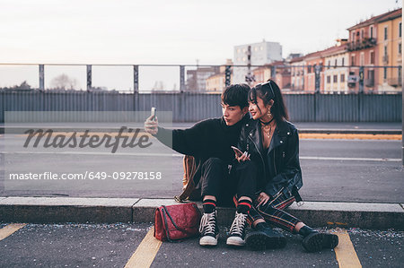 Young couple taking selfie on kerb, Milan, Italy