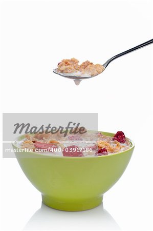 Cornflakes with fruits on the spoon above the green bowl. Shallow DOF