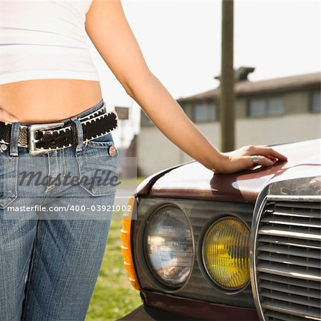 Midsection of young Caucasian woman standing beside automobile.