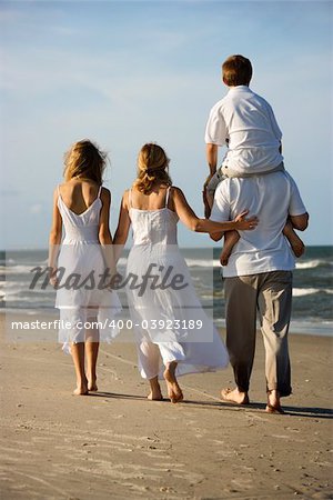 Caucasian family of four walking on beach with dad carrying son on shoulders.