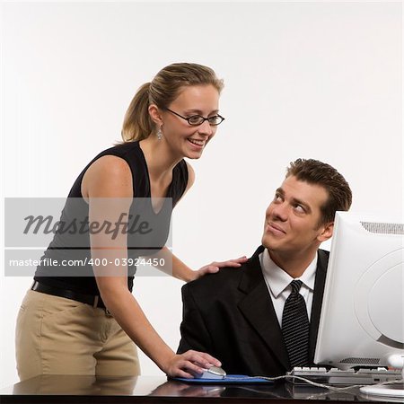 Caucasian mid-adult woman touching mid-adult man's shoulder and using mouse at computer.