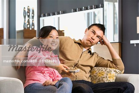 Asian couple sitting on couch watching TV.