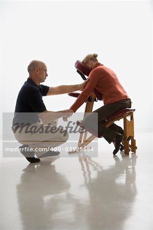 Caucasian middle-aged male massage therapist massaging arms and hands of Caucasian middle-aged woman sitting in massage chair.