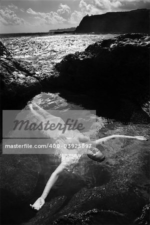 Young nude Asian woman floating in water with arms outstretched in Maui, Hawaii.