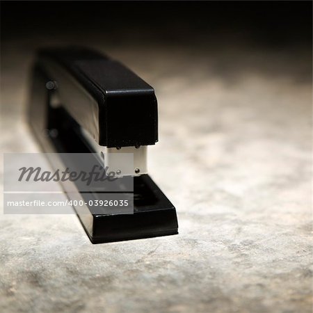 Black stapler on textured background.