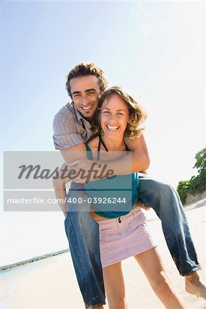 Mid-adult Caucasian woman giving man piggyback ride on beach.