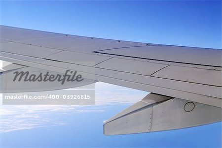 Wing of an airborne airplane with blue sky and ocean below