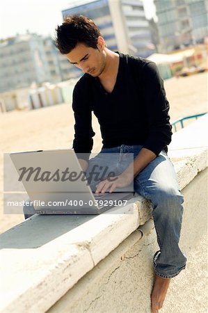 Young cool handsome man uses a personal computer sitting outdoor