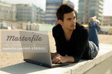 Attractive young man working at the beach with a laptop