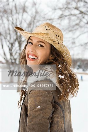 Caucasian young adult female outdoors in snow smiling at viewer wearing straw cowboy hat.