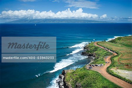 Aerial view of coastline with surfers and parked cars on Maui, Hawaii.