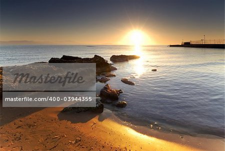 A very bright sunrise over a Mediterranean rocky seascape.