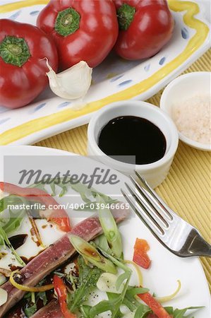 Finely sliced raw bleu beef with rocket and baby capsicum. Condiments of Murray River pink salt flakes and soy. Baby capsicum or peppers and garlic on a ceramic plate.