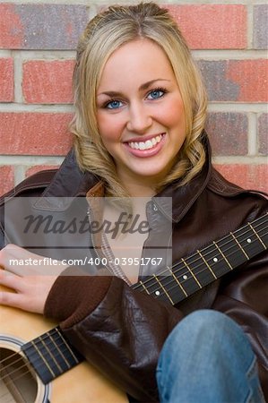 A beautiful, blue eyed young woman resting on an acoustic guitar.