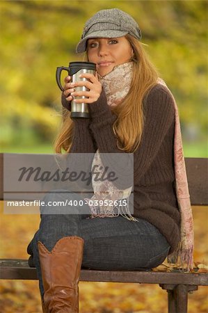 20-25 years old beautiful sexy woman portrait in natural autumn outdoors. Sitting on park bench with cup of coffee