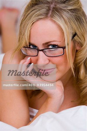 A beautiful young blonde woman looking naked in bed except for white bed sheets and glasses
