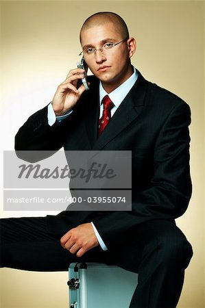 A businessman wearing black suit, using cell phone and sitting on case