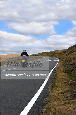 Lone motorbike rider on an uphill mountain road in the Brecon Beacons National Park, Wales, United Kingdom.