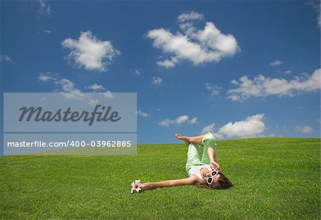 Beautiful young woman laying down on a green meadow with a flower