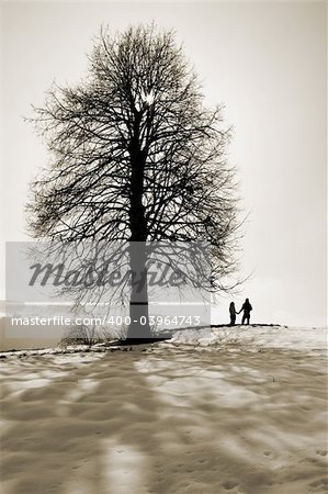 A couple holding hands under a tree in snow. Sepia tone.