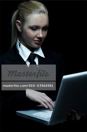 Beautiful business woman wearing black tie and jacket isolated on black background with laptop computer