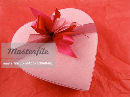 Pink heart-shaped chocolate box on a red tissue paper background