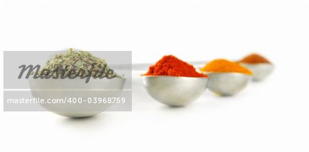Assorted spices in metal measuring spoons on white background