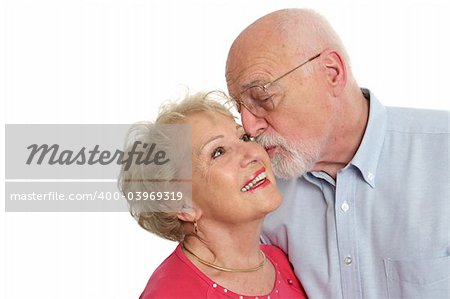 An attractive senior man kissing his beautiful wife on the cheek.  Isolated with room for text.