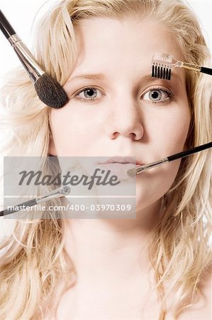 Studio portrait of a blond young lady with several make-up brushes on her face