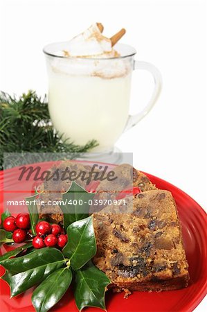 Closeup of delicious Christmas fruitcake garnished with Holly and a mug of egg nog in the background.  Isolated on white.