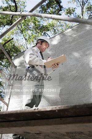 A building inspector on scaffolding inspecting the outside second story of a newly constructed building.