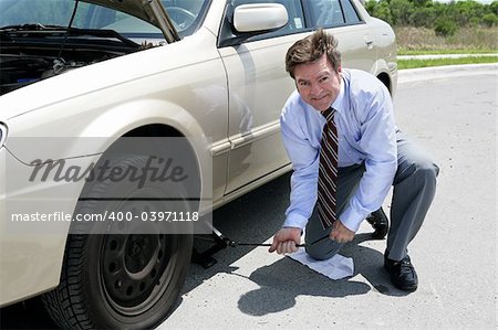 A businessman demonstrating how to use a jack to change a tire.