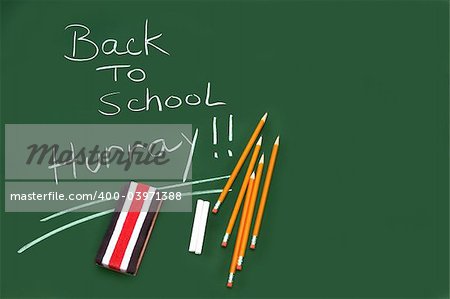 Back to school written on green chalkboard with pencils and eraser