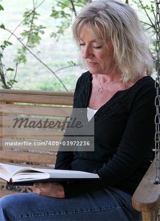 A beautiful mature woman relaxing and reading on her porch swing.