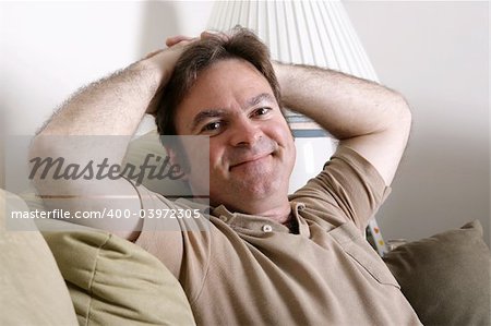 A handsome, friendly man relaxing at home with his hands behind his head.