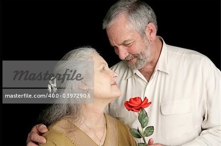 A beautiful mature woman receiving a red rose from her loving husband.  Focus on wife.  Black background