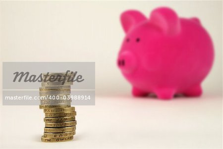 A stack of coins (GBP) and a piggy bank in the background.