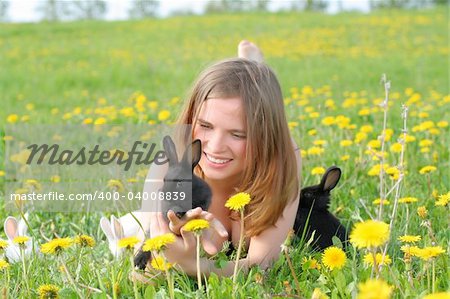 Beautiful young girl lays in grass and plays with cute small rabbits